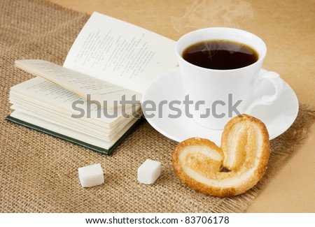 Cup of hot coffee with sugar, cake, spoon and book