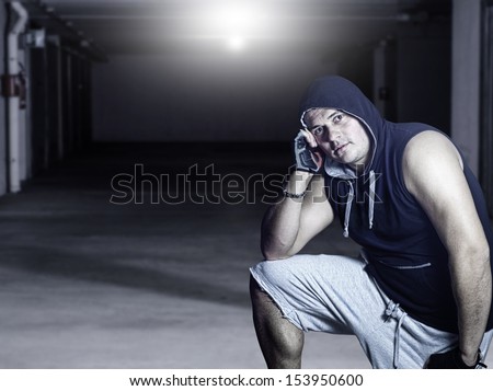 Young handsome man with hood in industrial garage looking at camera and resting head on arm.