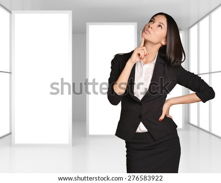 Girl standing on background of light interior with large blank posters and thinking looking up.