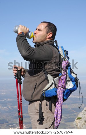 A handsome middle age hispanic latin man in a top of a in mountain hiking drinking some water