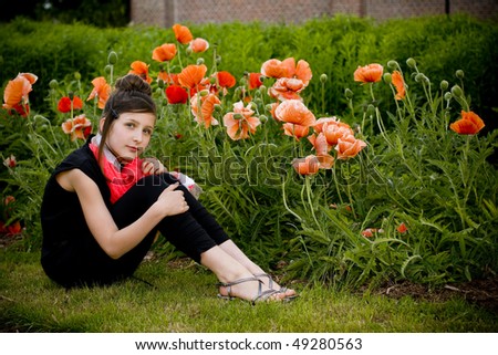 Teenage fashion girl with red scarf in a park with red poppies