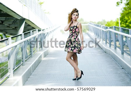 Teenager girl model presenting clothes on a bridge in the parc, light natural background