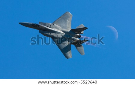 A fighter plane moves through the air against a bright blue sky with the moon visible.