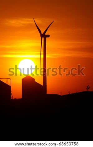 Agricultural silos of grain operation and turbines from a wind farm silhouetted by setting sun