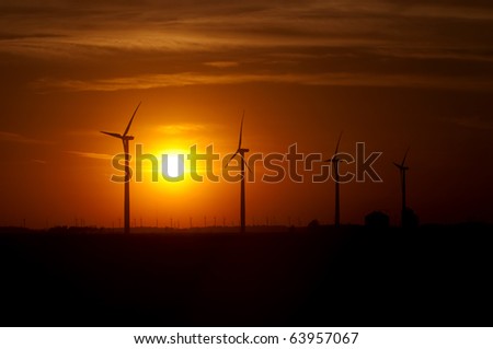Agricultural silos of grain operation and turbines from a wind farm silhouetted by setting sun