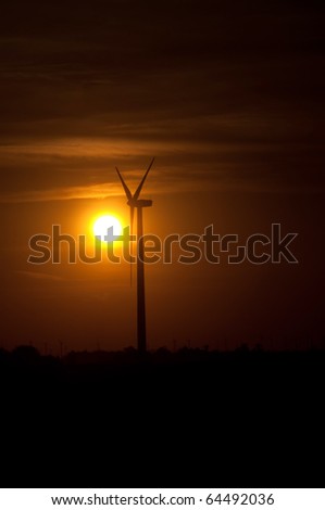 A wind turbine is silhouetted by the setting sun