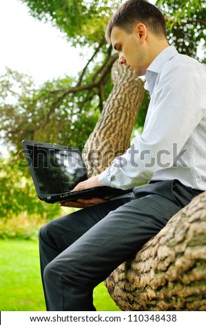 Happy man sitting outdoors using a laptop computer with a screen left blank for your image