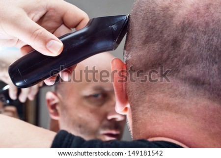 Man in the mirror cuts her hair with a razor