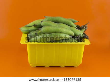 broad bean pods and beans on orange background .