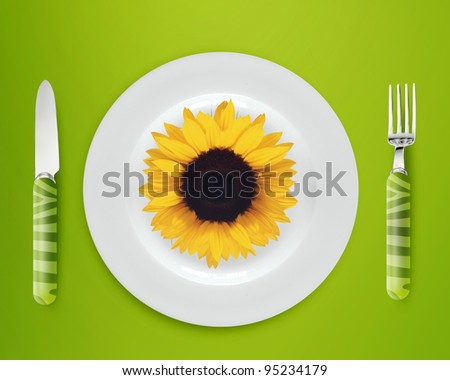 sunflower on white plate with knife and fork on blue background.