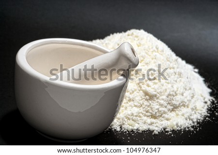 Small ceramic mortar and pestle with fine ground white powder ingredient after grinding for traditional medicine preparation on an apothecary shop counter