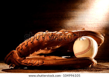 Old worn leather baseball catcher sport glove and aged stitched ball on antique wood boards in soft nostalgic Americana light