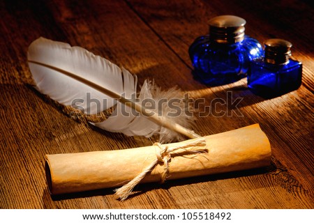 Antique parchment paper sheets roll tied by a string with and old ink writing feather quill and vintage colonial blue glass inkwells on a distressed ancient wood desk
