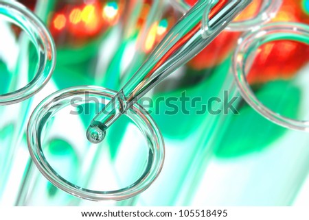 Laboratory pipette with drop of liquid over glass test tubes for a scientific experiment in a science research lab
