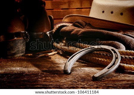 American West rodeo old horseshoe on lariat lasso and roping work gloves with Western horse rider gear with hat and aged leather roper boots on antique wood boars in a ranch barn