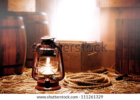 Old kerosene lantern lamp and aged rope with shipping crates containers and packaging boxes near transportation wood barrels in soft fog diffused light on an ancient port vintage wooden shipping dock