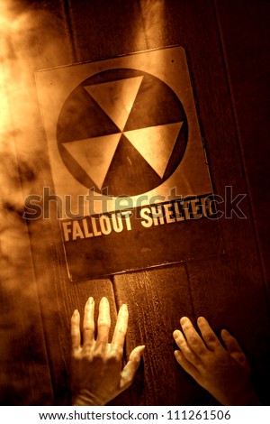 Gruesome and tragic nuclear disaster catastrophe scene with dead victims hands reaching for emergency fallout shelter sign in fire smoke in rough grunge sepia