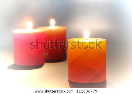 Elegant yellow decorative marbleized pillar candle burning with a soft glow flame in smoke with lit red and green candles relaxation and for a soft relaxing mood