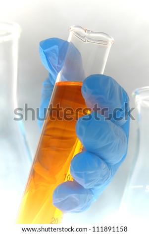 Scientist hand holding a scientific cylinder filled with amber liquid for a scientific experiment in a science research lab
