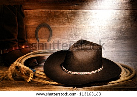 American West rodeo cowboy black felt hat on an authentic Western roping lariat lasso with leather riding boots on weathered wood floor in an old ranch barn