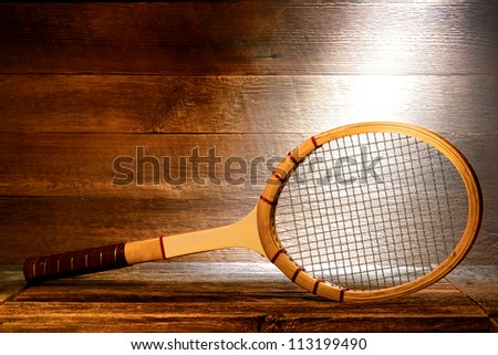 Vintage wood tennis racket on aged wooden plank floor in a dusty old house attic lit by soft diffused sunlight through a window