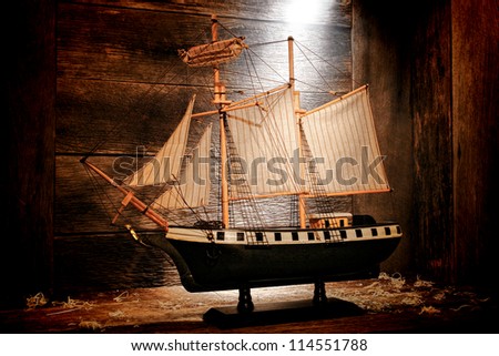Antique wooden miniature toy reproduction model war navy sail ship with nostalgic aged canvas sails in an old wood attic lit by diffused dusty light