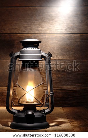 Old fashioned rustic kerosene oil lantern lamp burning with a soft glow light in an antique country barn