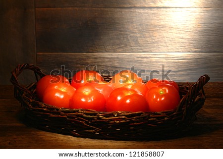Organic fresh tomatoes in an old wicker basket on a traditional country farm produce stand wood table in a vintage rural barn lit by soft diffused sunlight