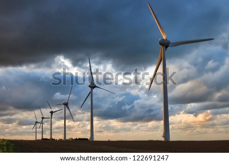 Renewable alternative energy wind turbines farm with electric power generation windmills towers generating clean environmentally friendly electricity over evening sky
