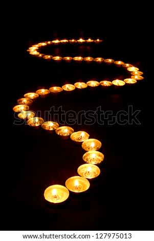 Lit meditation candles burning with soft glowing flame forming a Zen inspired curved path on black a surface for prayer and reflection in a spiritual retreat temple