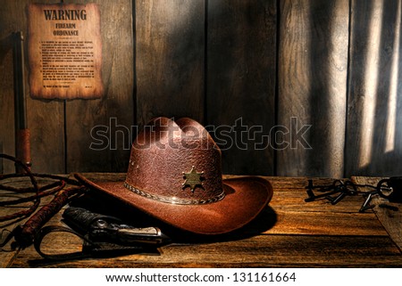 American West legend brown felt western cowboy hat on aged wood table sheriff desk with old lawman gun in holster and bullwhip in a dark county jail