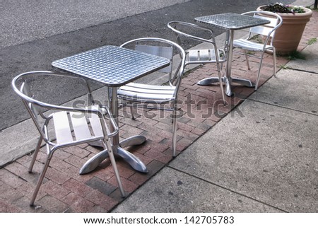 Retro style stainless steel restaurant tables and chairs on an old city street sidewalk in front of an outdoor cafe terrace