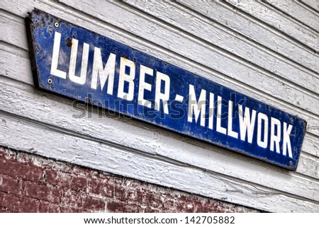 Old and distressed lumber millwork antique advertising enamel sign hanging on a vintage lumberyard wood clapboard wall