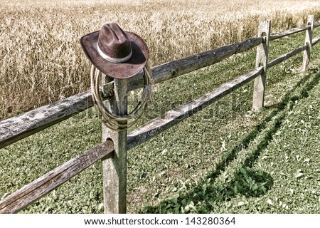 American West rodeo cowboy brown hat and roping lasso lariat hanging on an old wood fence post on a western ranch field