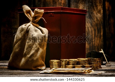 American west legend stacks of gold coins and paper money bills with valuable bag and steel strongbox with vintage lock and key on an old Western office wood table ready for shipment to a deposit bank