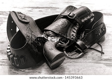 American West legend revolver style old six-shooter gun in antique cowboy leather holster on grunge aged wood planks