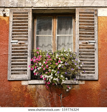 Old house window with antique wood shutters and hanging flowers on a vintage French house in a small village in France