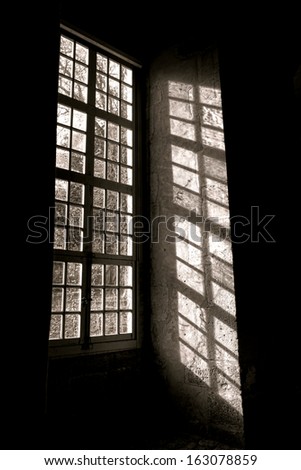 Bright sunlight filtering through the old leaded glass of an antique wood window and drawing a shadow pattern of muntin and mullion unto an ancient interior wall inside a historic buidling