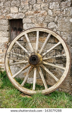 Antique and weathered wood cart wagon wheel with vintage wooden spokes leaning against an old stone farm building wall