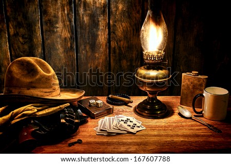 American West Legend Cowboy Hat And Gun In Holster On Old Western Hotel Room Nightstand Table With Vintage Poker Playing Cards And Kerosene Oil Lamp Everyday Items In Nostalgic Americana Scene
