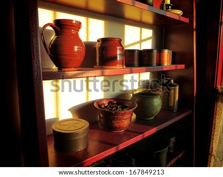 Antique household objects and collectible kitchen cooking items on old wood shelf in morning sun light filtering through a vintage window in a historic home