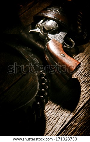 American West legend antique six-shooter revolver gun in vintage cowboy leather holster with old lead bullets on weathered wood plank western saloon table