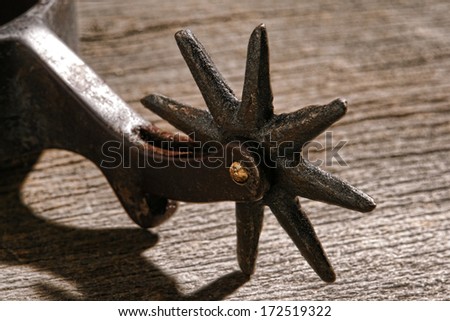 American West rodeo cowboy antique horse riding spur with old style star shape spikes rowel on weathered wood planks in a vintage western ranch barn