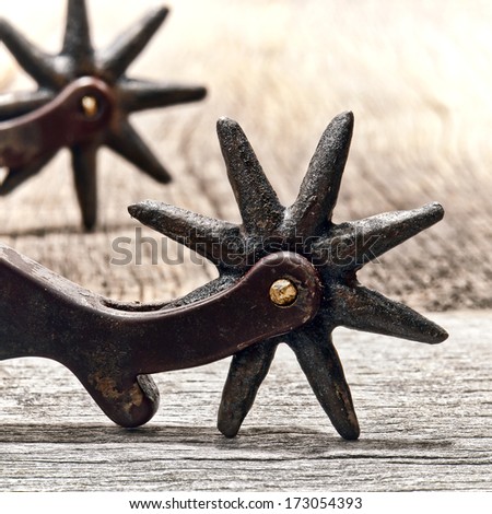 American West rodeo cowboy vintage horse riding spurs showing wear and tear with corrosion and rust with old style star shape spikes rowel on weathered wood boards in a vintage western ranch barn