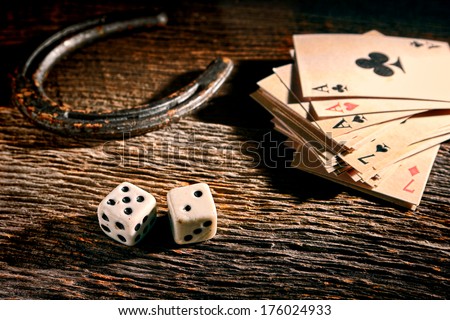 Lucky craps game dice rolling out chance number seven and vintage poker cards with winning aces by old horseshoe for player and gambler good luck charm on rustic wood table in western gambling saloon