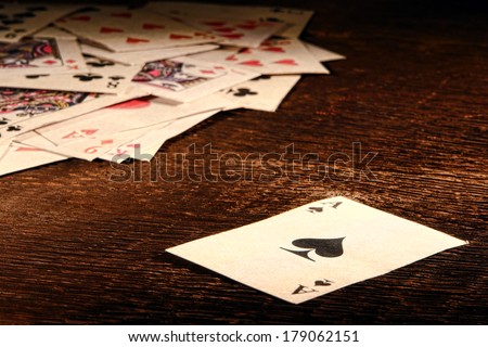 American West Legend vintage ace of spade playing card and stack of antique poker game cards on a weathered wood table in an old western frontier gambling establishment saloon