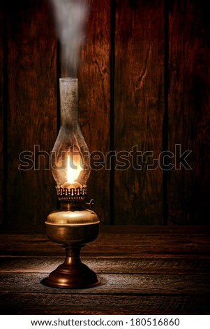 Antique rustic kerosene oil lantern lamp burning light with a soft glow flame making smoke on a vintage wood table in an old western ranch barn
