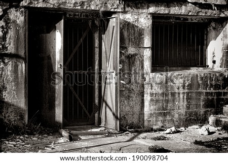 Vintage armored steel door entry with prison bars and reinforced jail window inside the damaged concrete walls of an abandoned fortified defense bunker in a deserted coastal artillery fort
