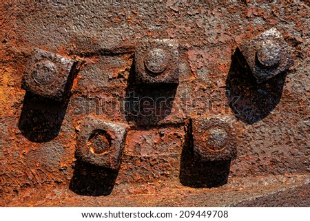 Antique rusty metal square nuts locked with rust and corrosion on old heavy duty bolts holding a thick and corroded vintage industrial steel plate structure as a retro grunge background