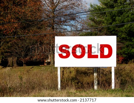 Real estate commercial size sold sign in a field advertising an empty lot for sale